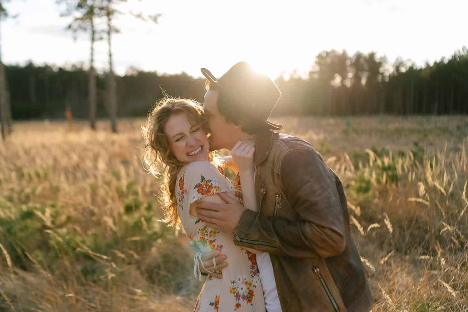 Junges Paar im Sonnenlicht auf Wiese, lachend, glücklich.