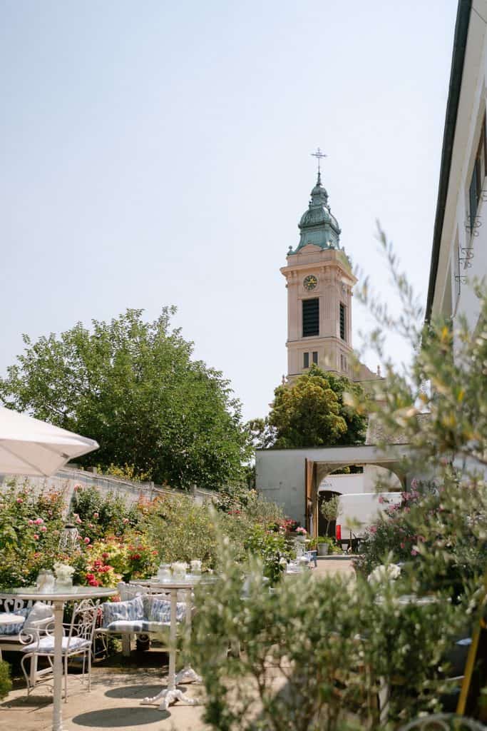 Gartencafé mit Blumen, weißen Tischen, Uhrturm, Hochzeit.