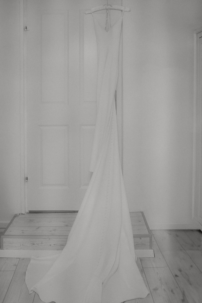 Weißes Brautkleid hängt vor der Tür, langer fließender Schnitt.