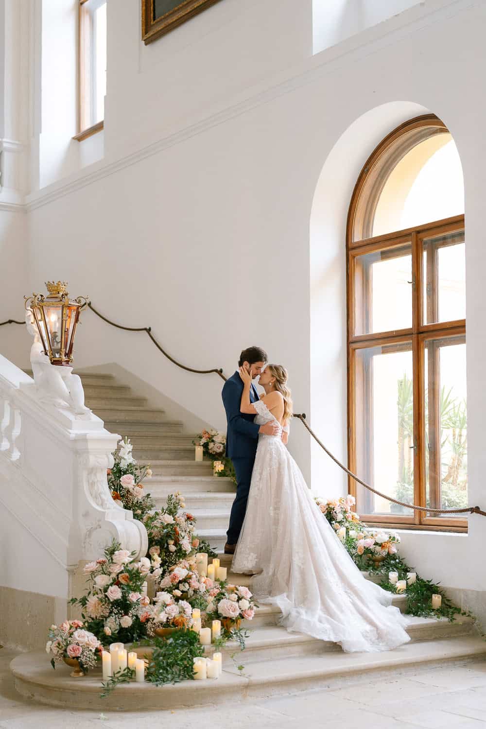 Braut und Bräutigam küssen sich auf blumengeschmückter Treppe im Schloss Eckartsau