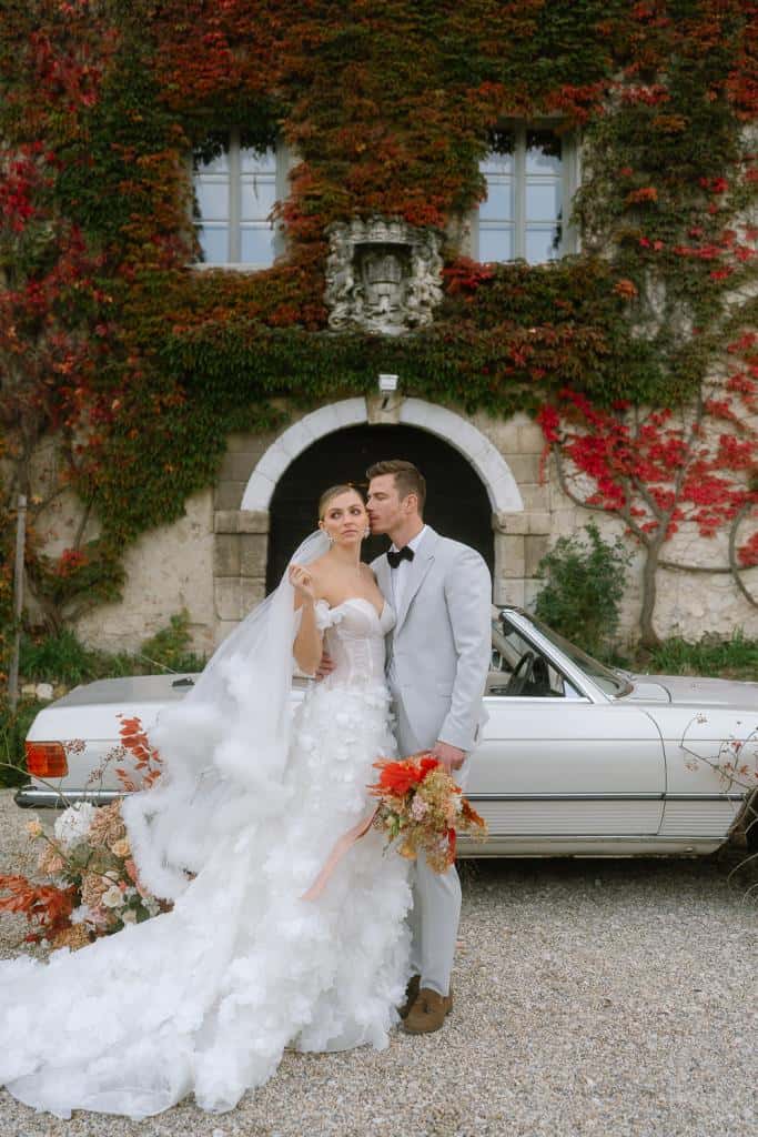 Brautpaar steht vor dem Schloss Hagenberg, neben einem Oldtimer