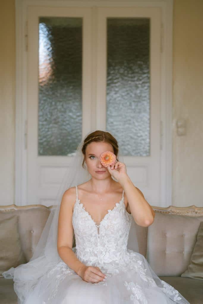 Braut im Spitzenhochzeitskleid hält Pfirsichblüte auf der Couch.