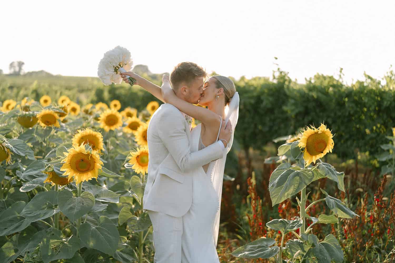 Brautpaar küsst sich im Sonnenblumenfeld. Hochzeit im Himmelblau