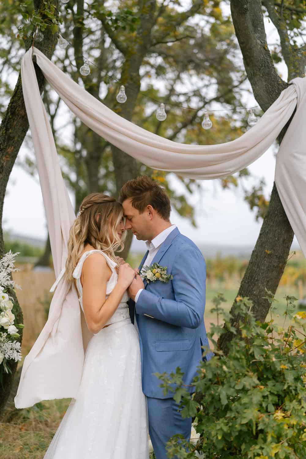 Braut und Bräutigam unter Lichterkette bei Outdoor-Hochzeit.