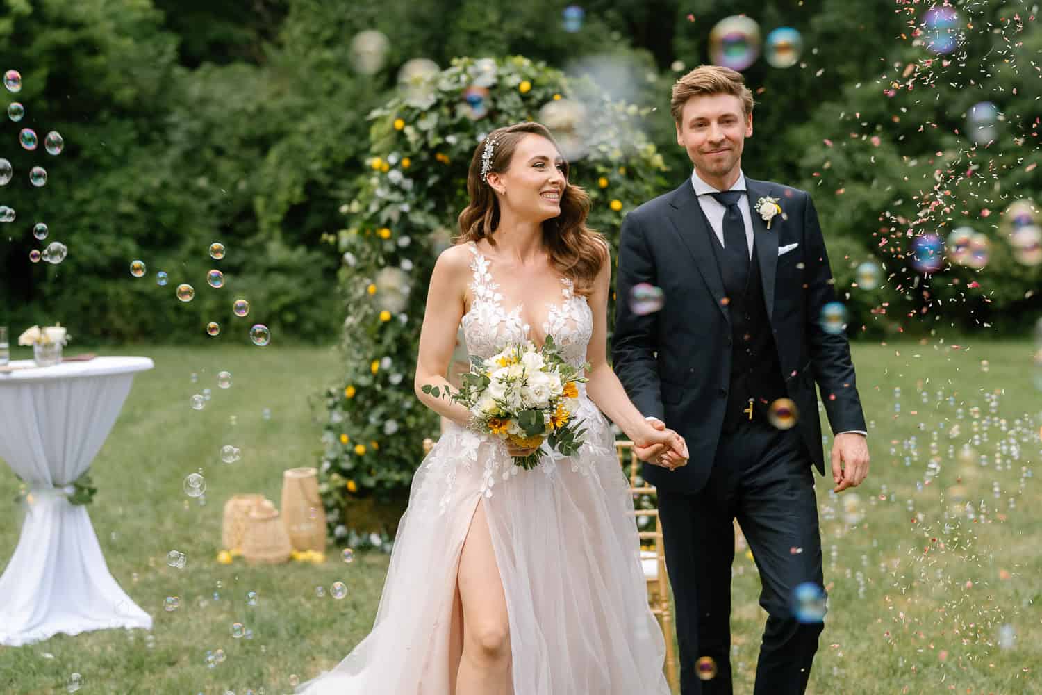 Hochzeitspaar lächelnd im Freien mit Blasen und Blumenbogen beim Schloss Nikitsch