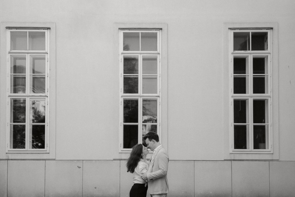 Paarshooting schwarz-weiß, romantisch vor Gebäude mit drei Fenstern.