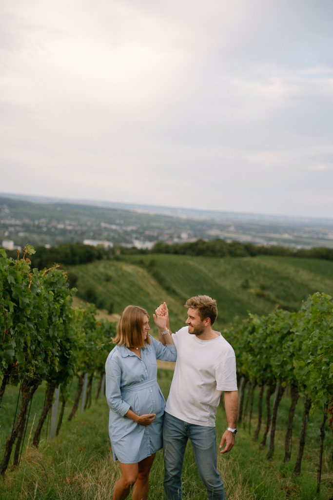 Paarshooting im Weinberg, schwanger, Händchen haltend, grüne Weinreben.
