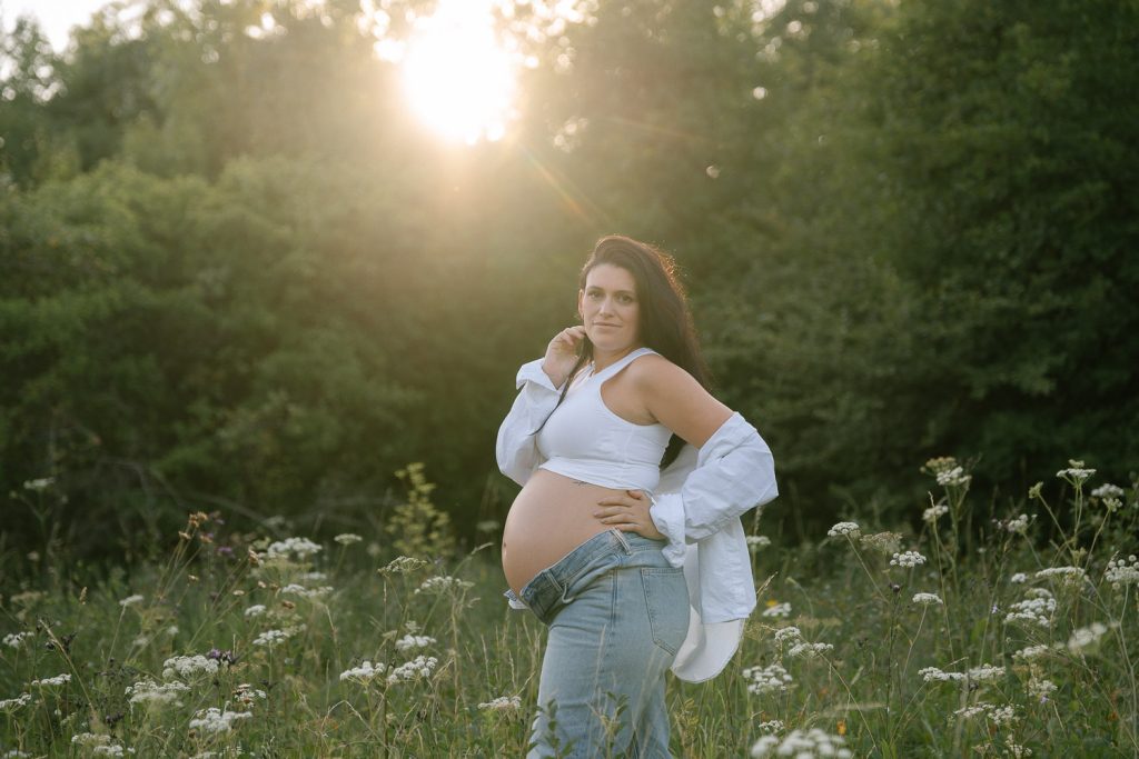 Schwangere Frau im Wildblumenfeld mit Jeans, Schwangerschafts-Shooting Outdoor.