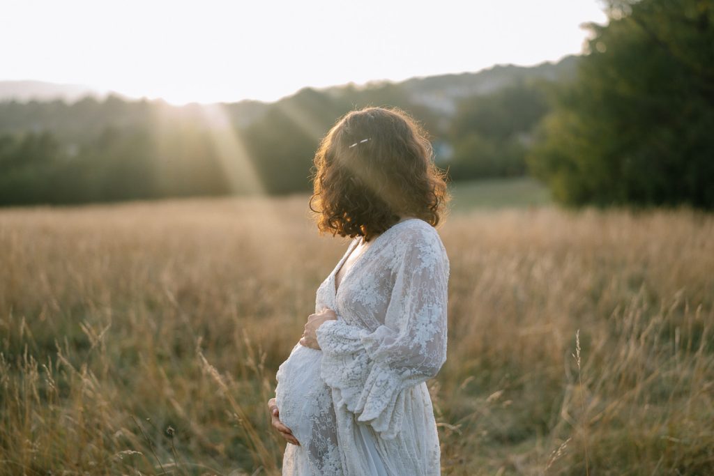 Schwangere Frau in weißem Spitzenkleid, Sonnenuntergang Mutterschaft Fotoshooting Feld.