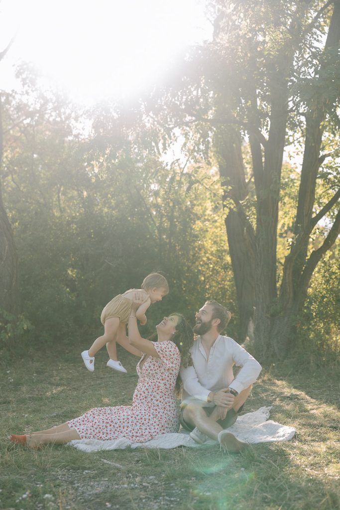 Familienfoto Outdoor-Shooting: Frau hebt lachendes Kind auf Picknickdecke.