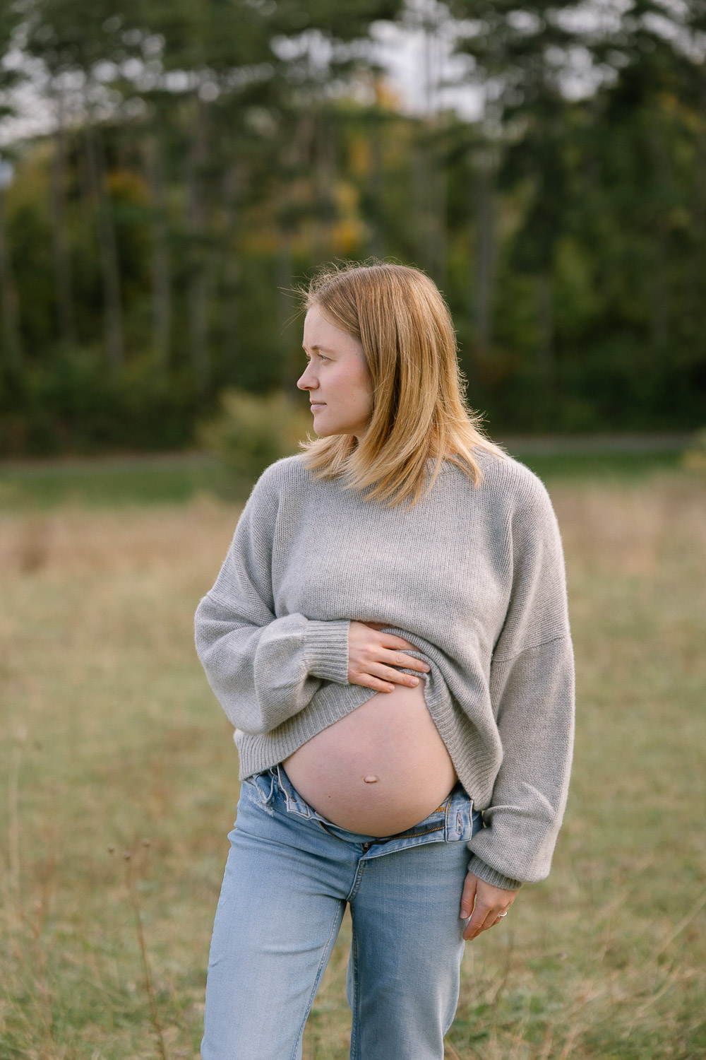 Schwangere Frau im Pullover zeigt stolz ihren Bauch beim Babybauchshooting in Wien