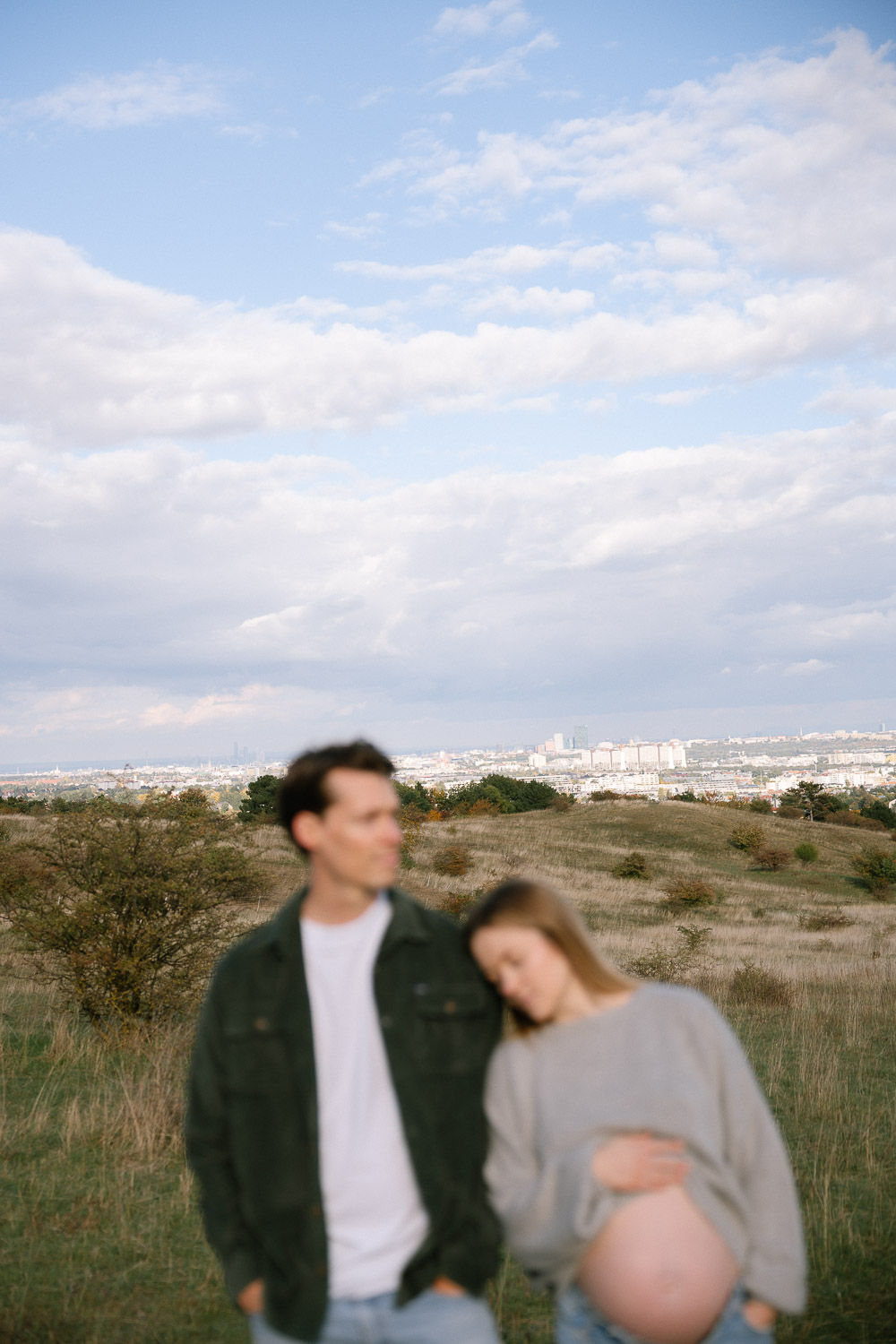 Babybauchfotos in der Natur mit Blick über Wien – Paar in entspannter Pose mit Stadtblick