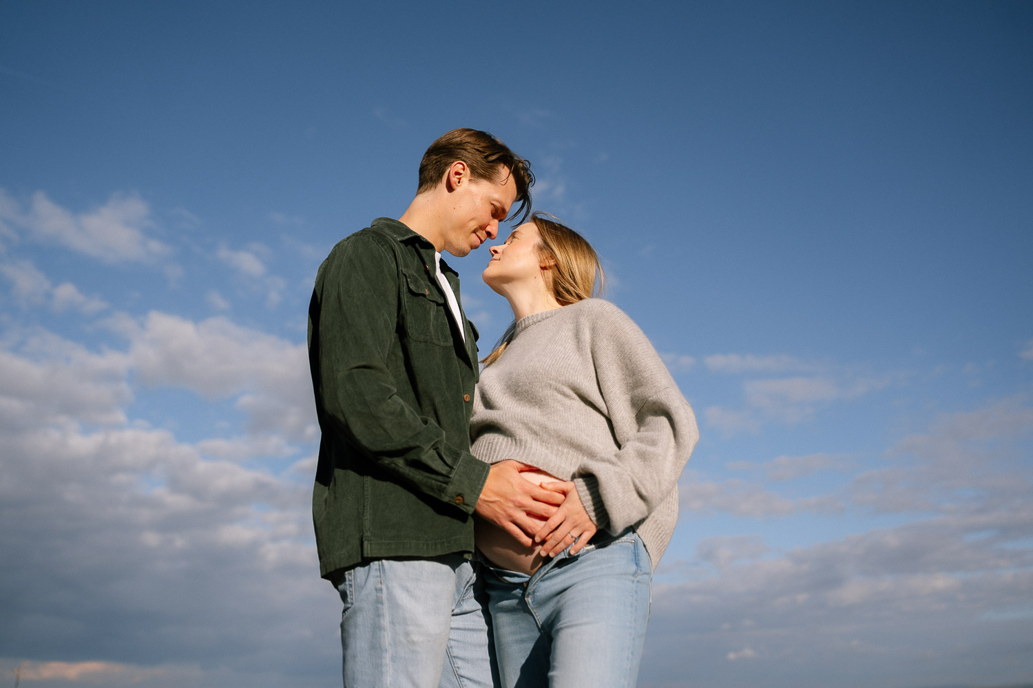 Natürliches Schwangerschaftsshooting in Wien – Paar blickt sich verliebt an unter blauem Himmel