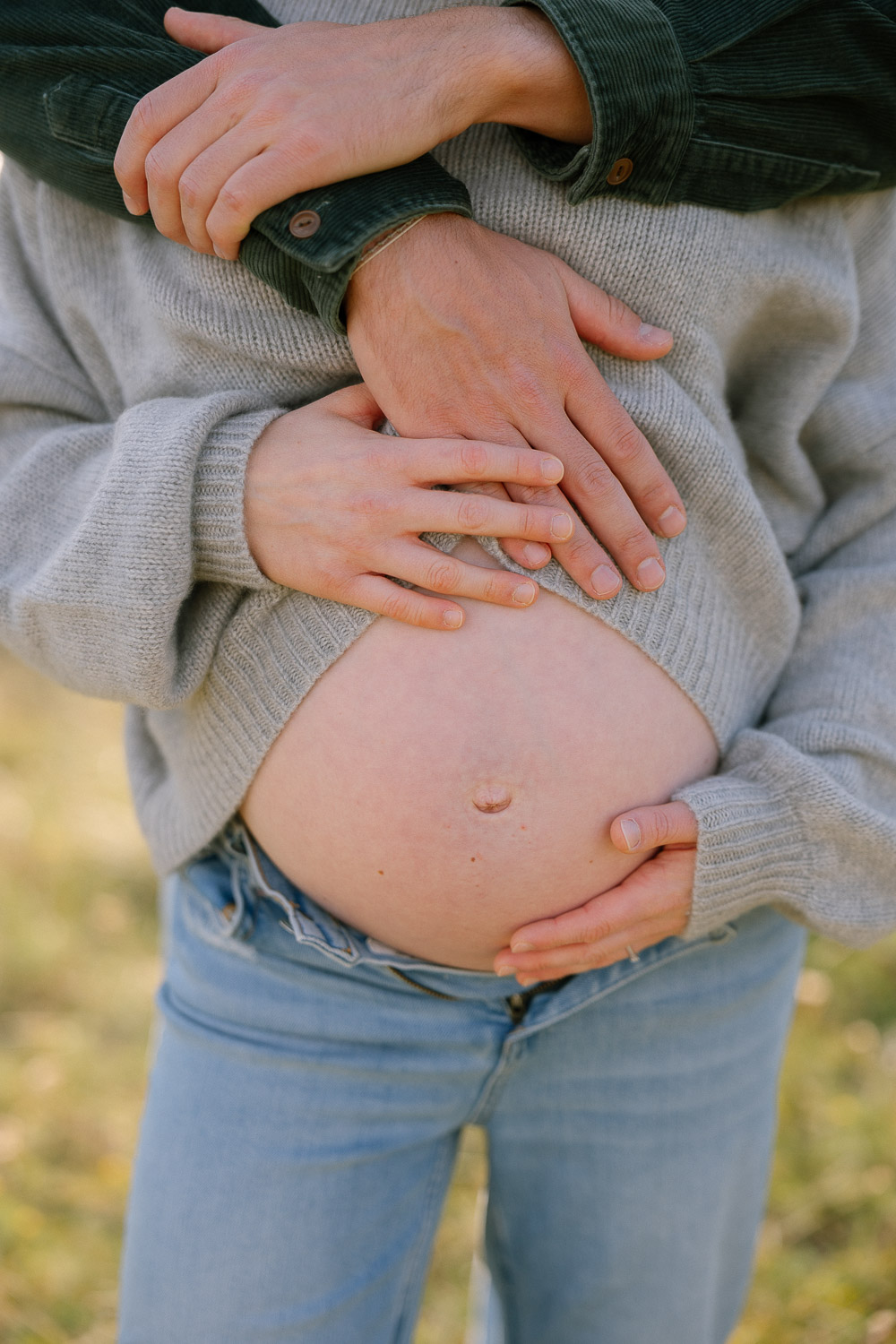 Detailaufnahme vom Babybauch – Hände der werdenden Eltern auf dem Bauch