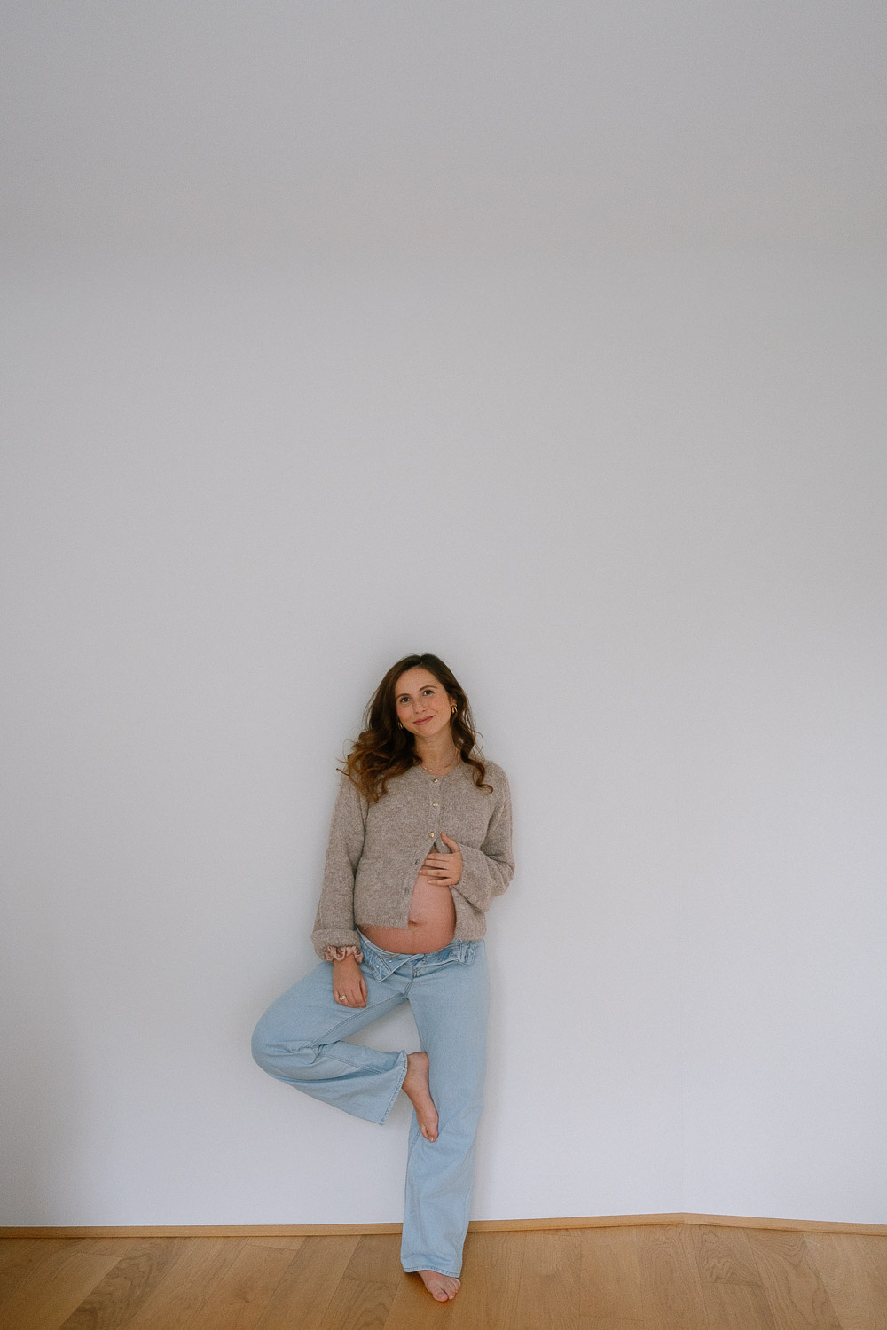 Schwangerschaftsfoto in Wien mit offener Jeans und sichtbarem Babybauch, lässige Pose