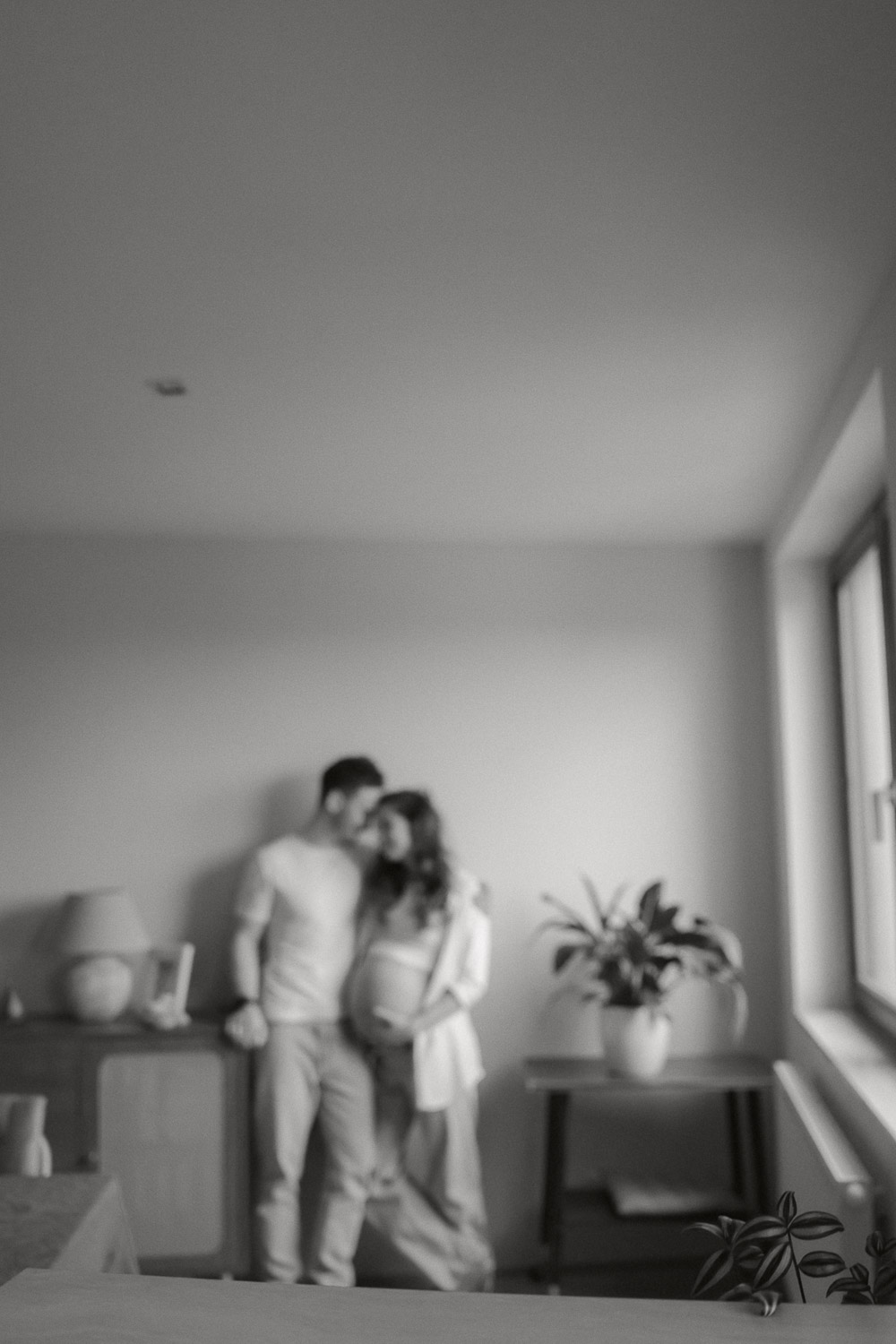 Künstlerisches Babybauchfoto in Wien mit unscharfem Paar, gemütliche Wohnzimmeratmosphäre