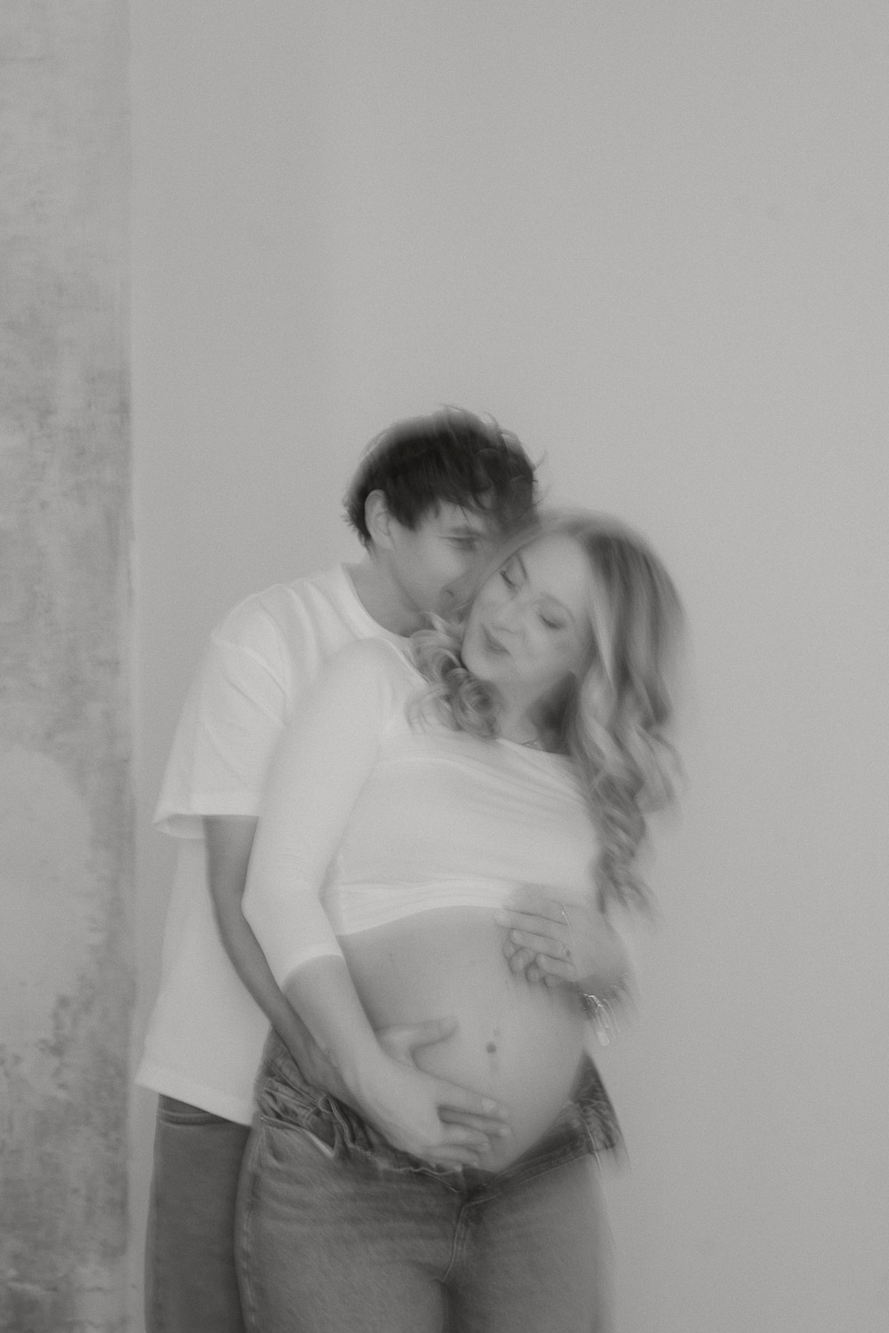 Verschwommenes Schwarz-Weiß-Foto eines verliebten Paares, das den Babybauch der Frau umarmt – emotionale Schwangerschaftsfotografie in Wien