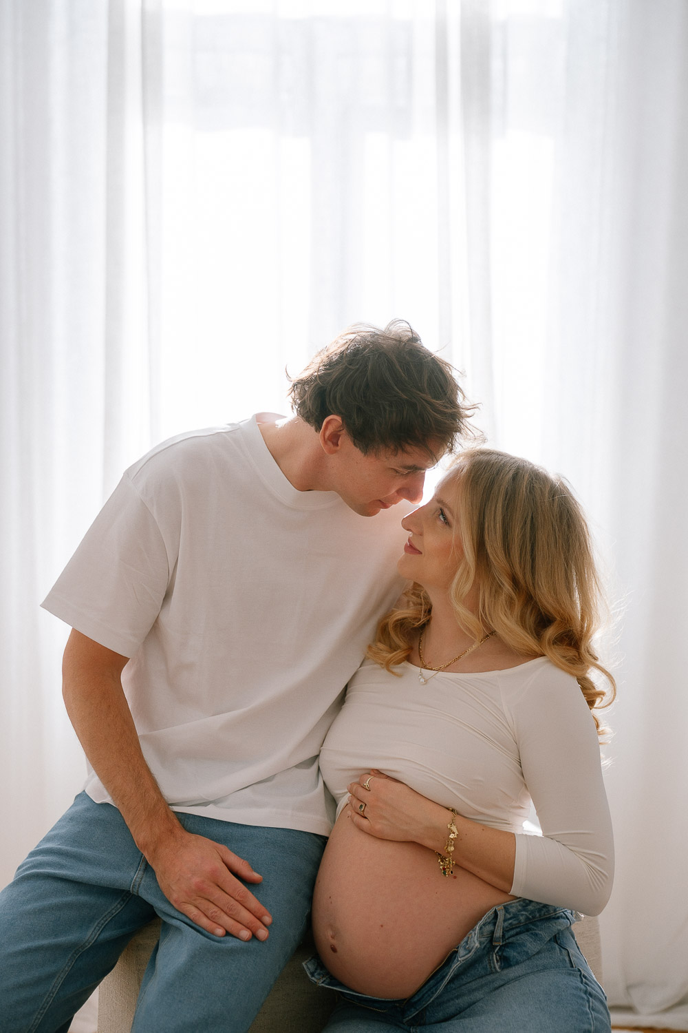 Intimer Moment zwischen werdenden Eltern im Gegenlicht vor Vorhängen – Schwangerschaftsfotografie mit natürlichem Licht in Wien