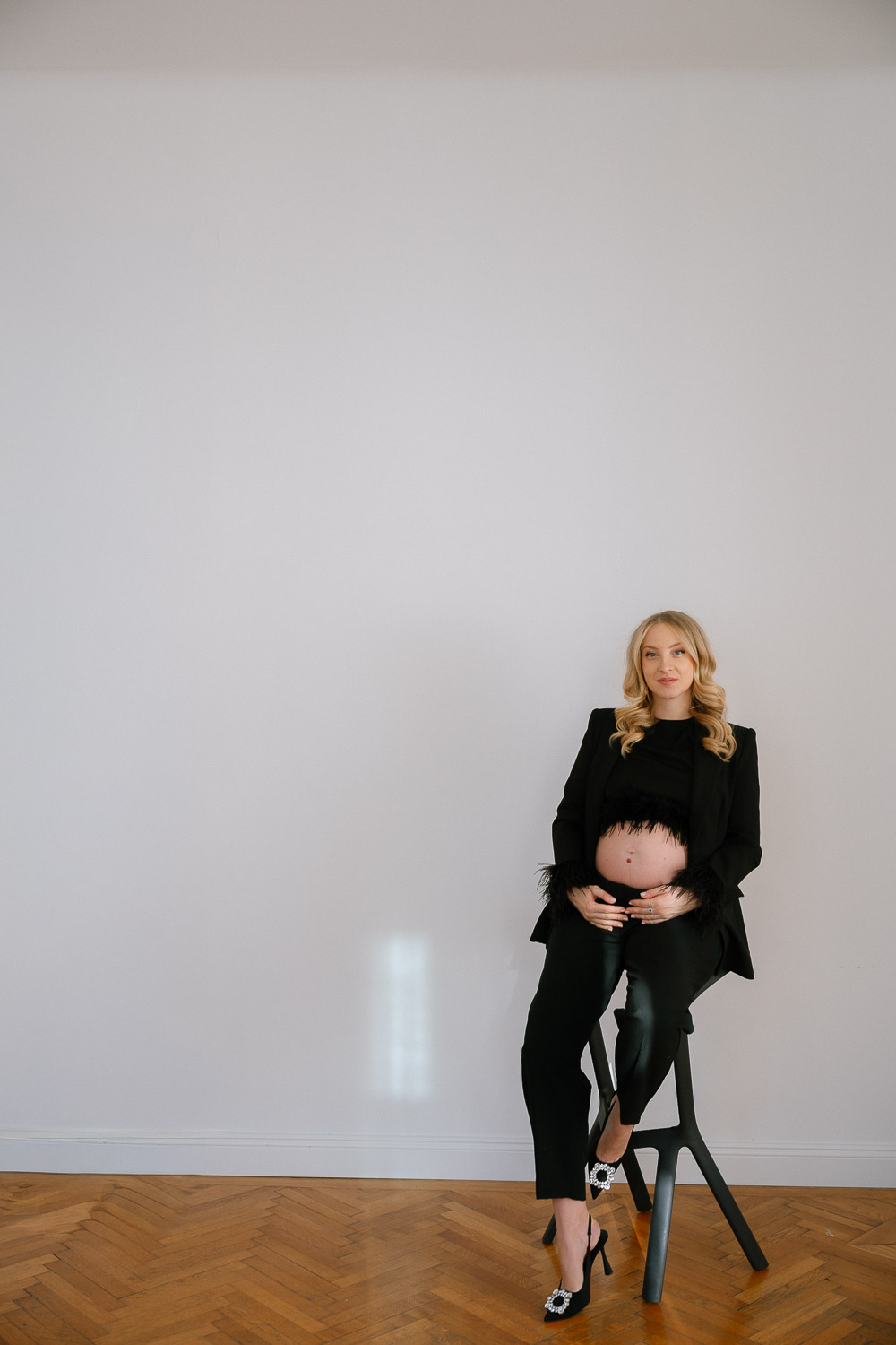 Elegante Schwangere im schwarzen Anzug auf einem Hocker – stilvolle Schwangerschaftsfotos in Wien
