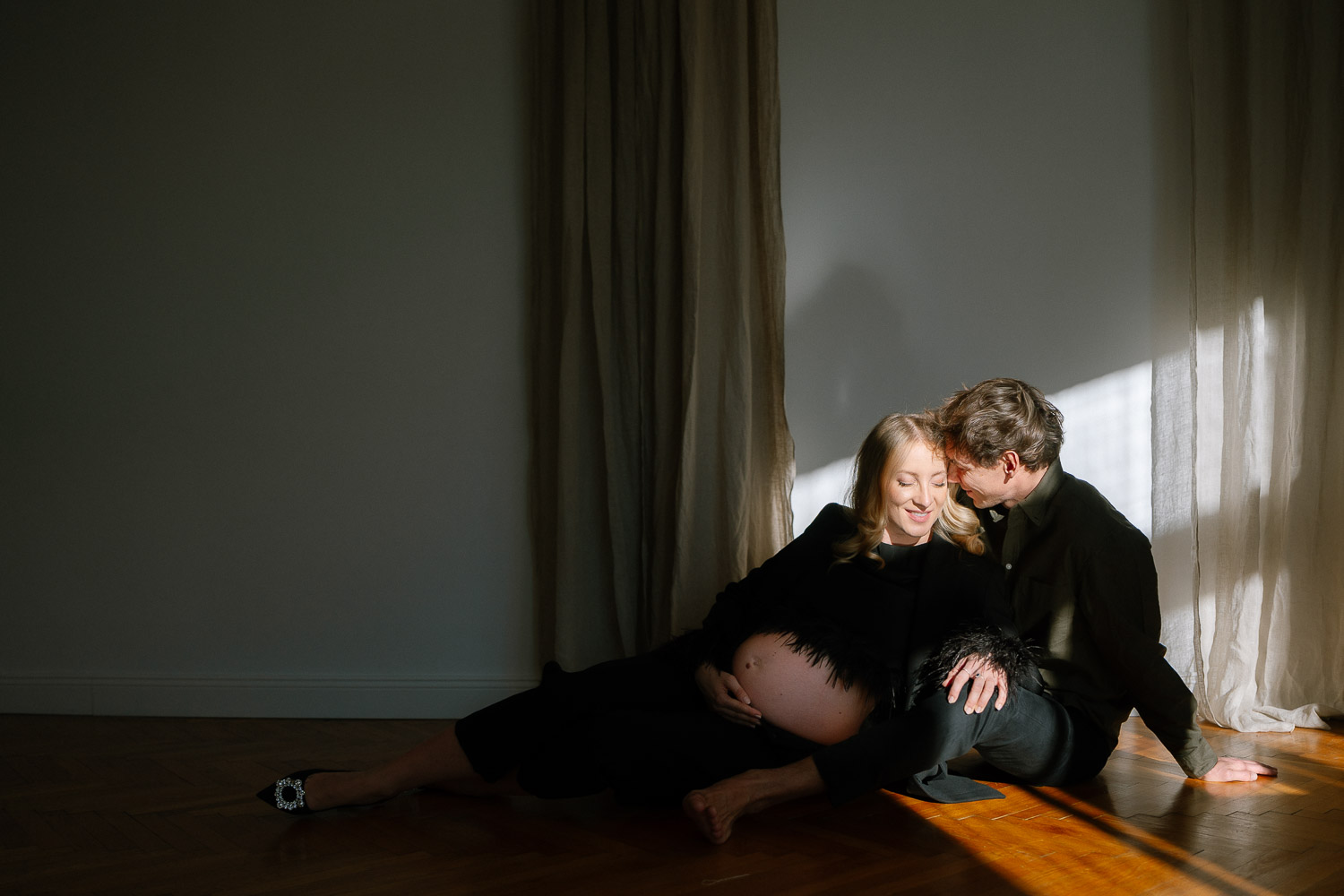 Intime Szene: Paar sitzt gemeinsam im Lichtstrahl auf dem Boden – natürliche Schwangerschaftsfotografie mit Tiefe
