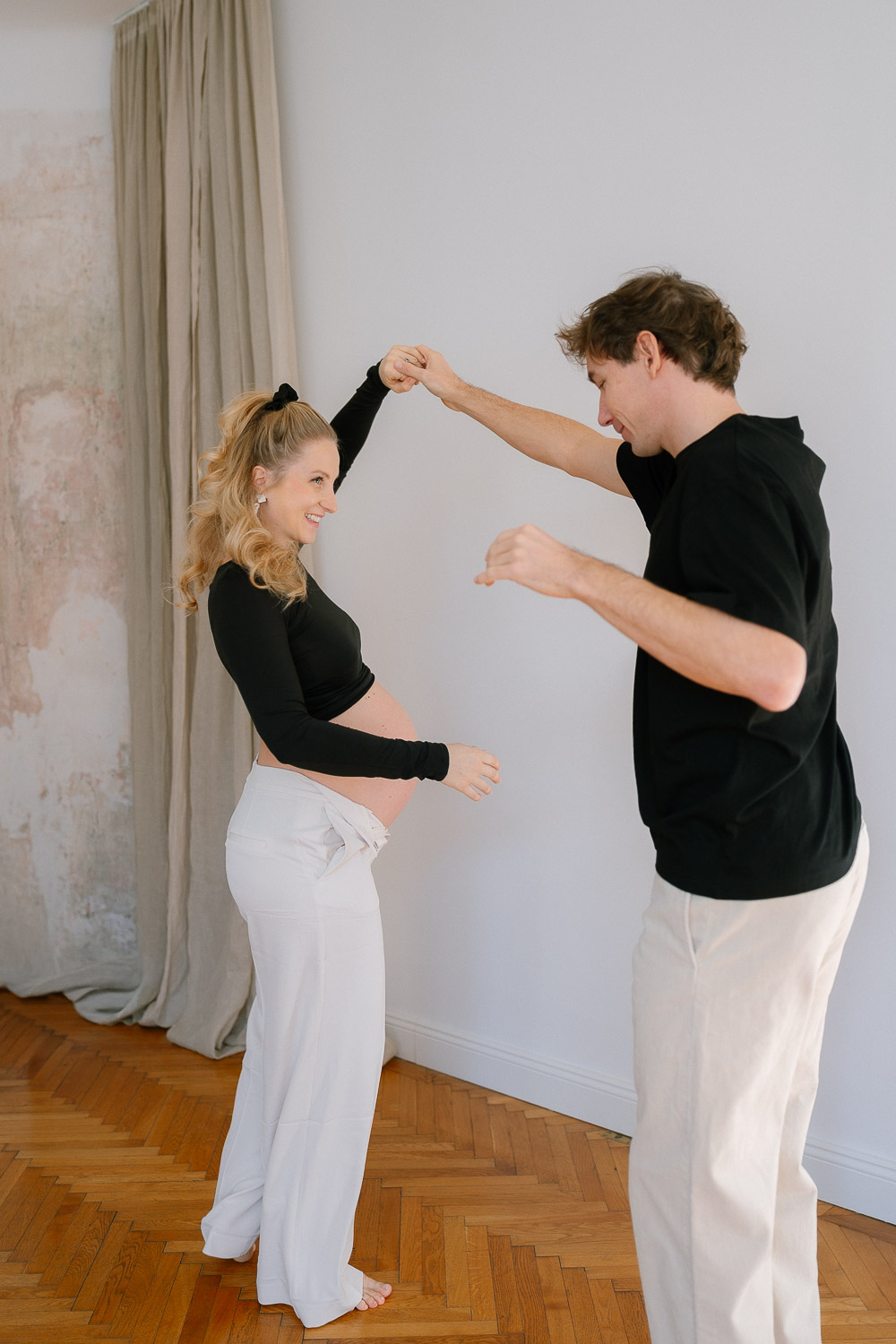 Schwangere Frau tanzt barfuß mit ihrem Partner im hellen Wohnzimmer – fröhlicher Moment voller Leichtigkeit.