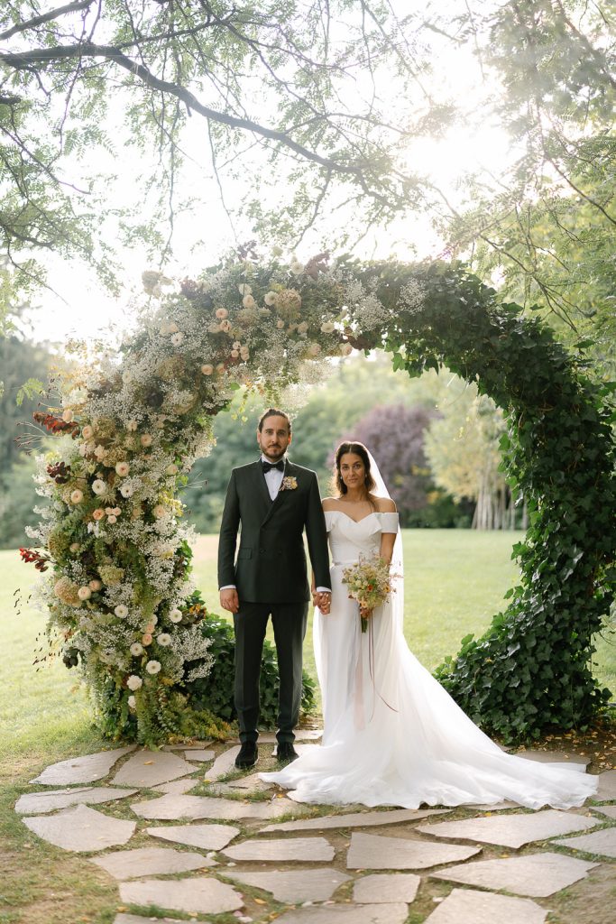Braut und Bräutigam stehen Hand in Hand unter einem mit Blumen geschmückten Bogen bei ihrer Hochzeit in Graz