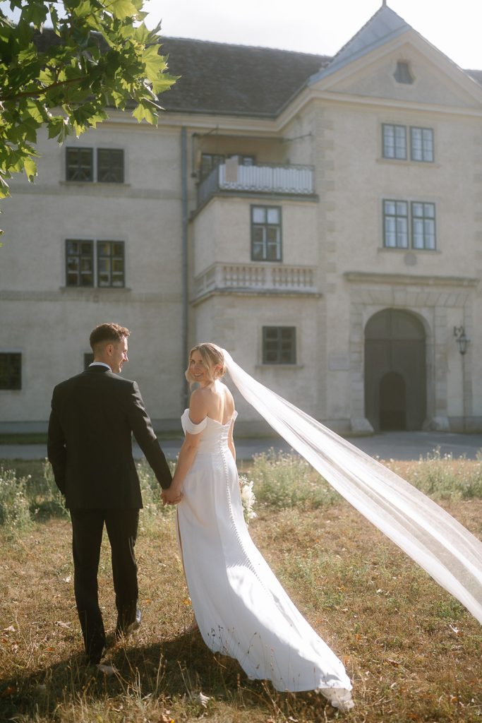 Die Braut wirft den Schleier im Sonnenlicht, elegant vor dem Schloss