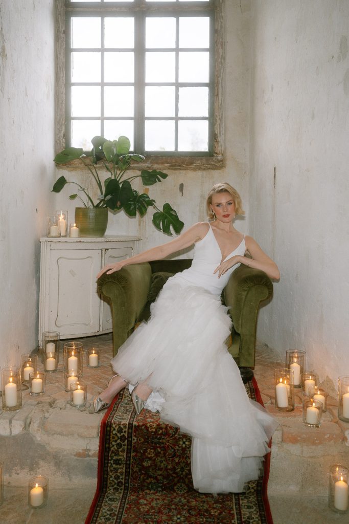 Die Braut sitzt in einem grünen Sessel, umgeben von Dutzenden Kerzen – romantisches Setting im Schloss Haggenberg