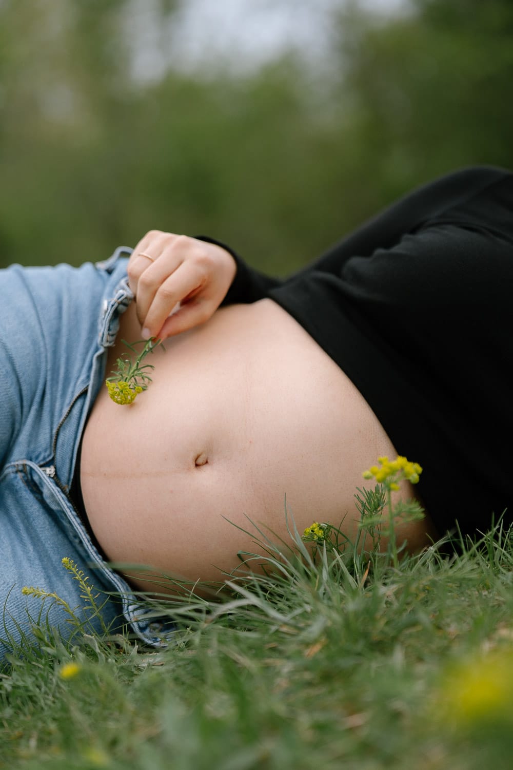 Detailfoto eines Babybauchs bei einem natürlichen Babybauch Shooting in Wien mit kleiner gelber Blume